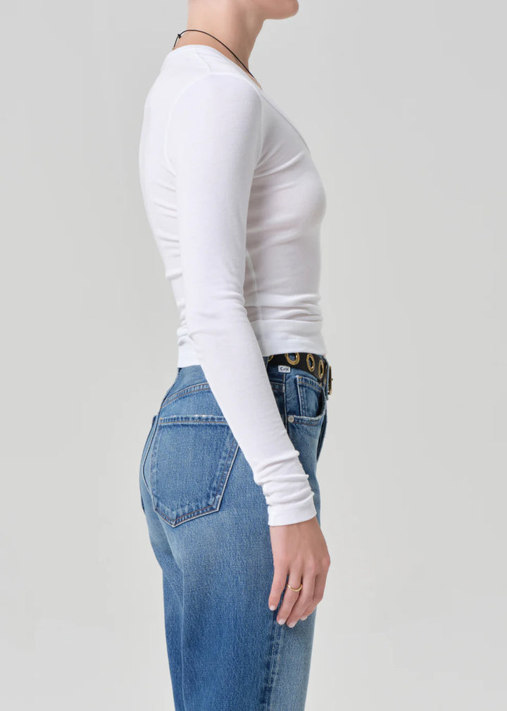 Person wearing a white long-sleeve top and blue jeans on a plain background