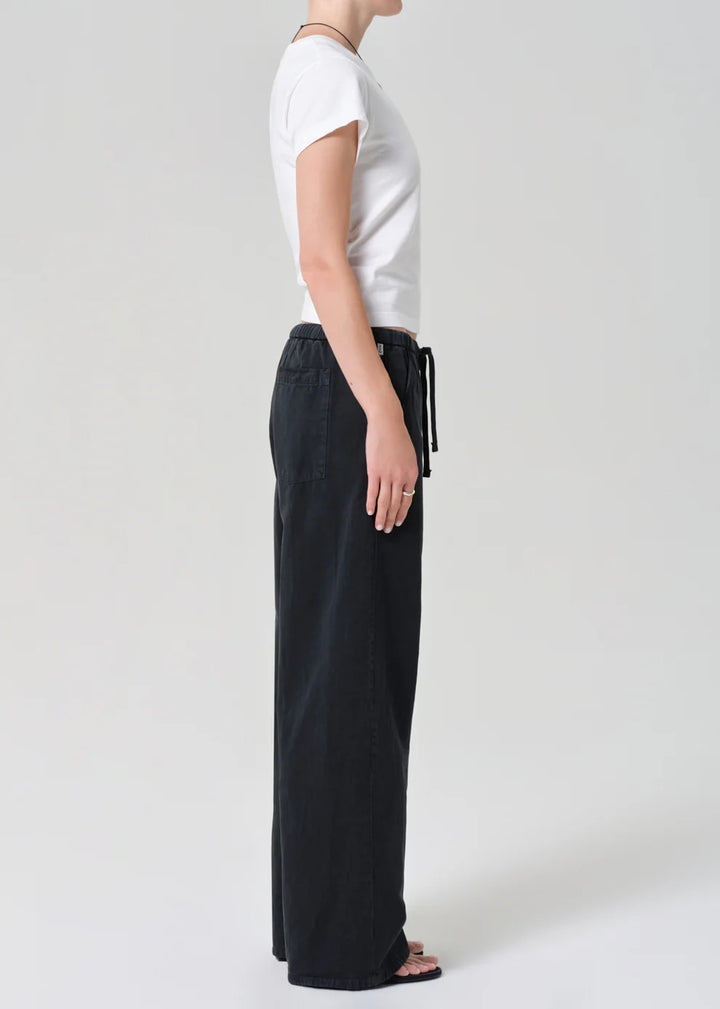 Person wearing a white t-shirt and black pants on a plain background