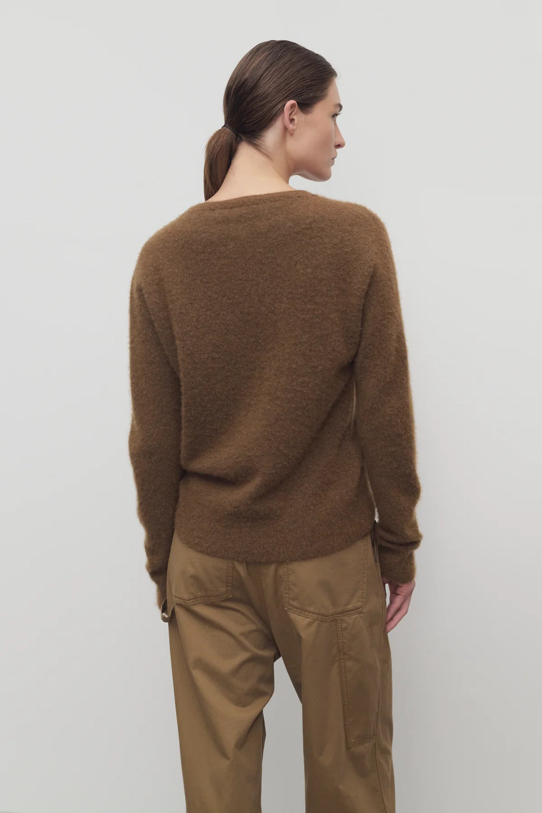 Person wearing a brown sweater and pants against a white background