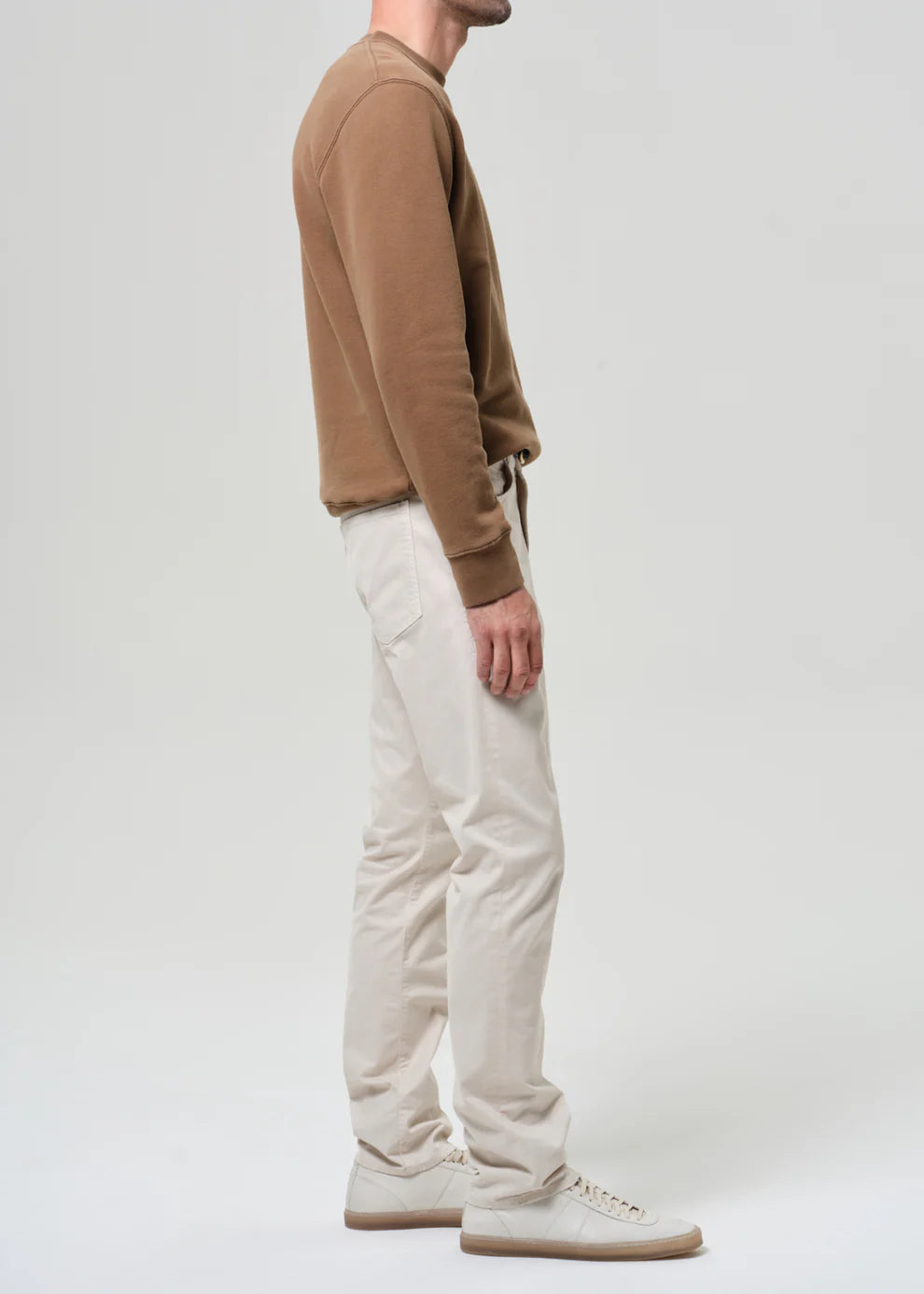Person wearing a brown sweater and white pants on a plain background