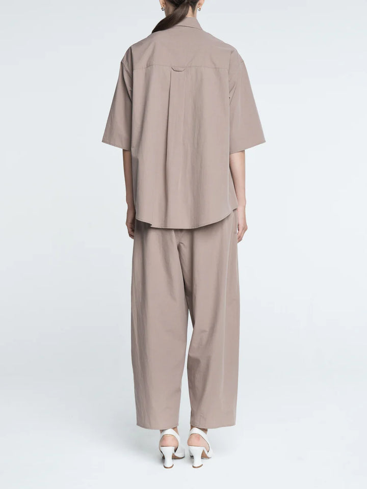 Person wearing a beige outfit with a shirt and pants on a white background