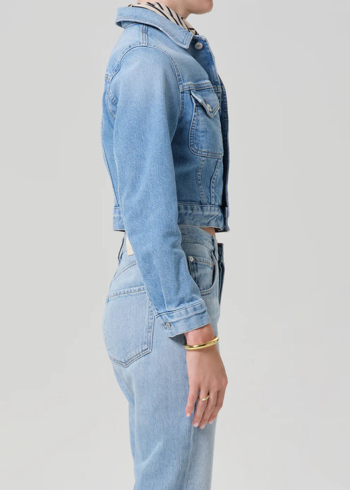 Person wearing a light blue denim jacket and jeans on a plain background