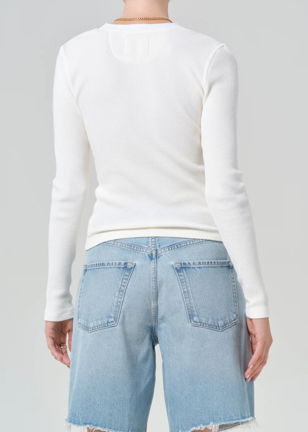 Person wearing a white long-sleeve shirt and light blue jeans on a gray background