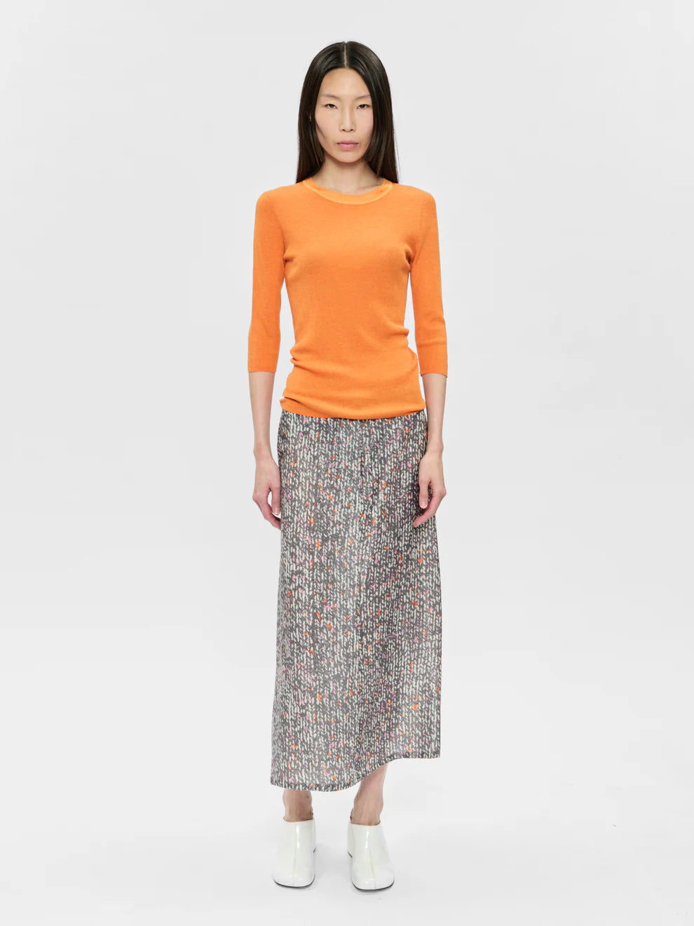 Woman wearing an orange sweater and patterned skirt on a white background