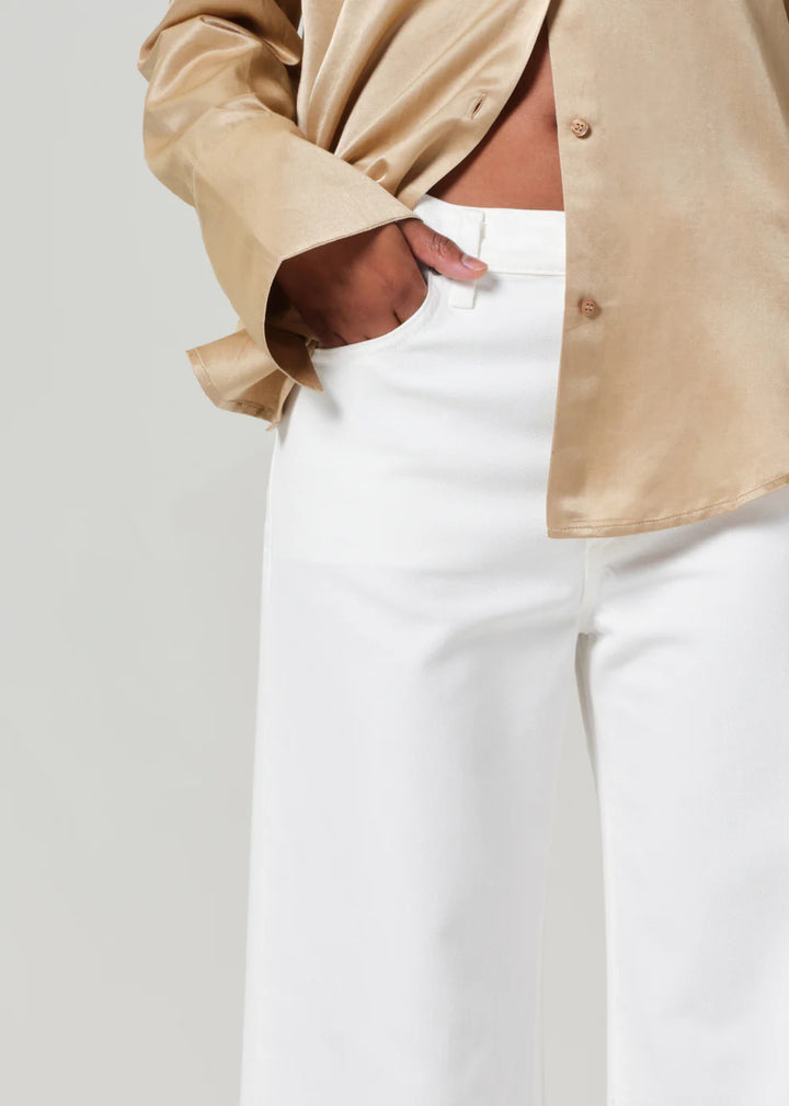 Person wearing a beige shirt over a white top and pants on a light gray background