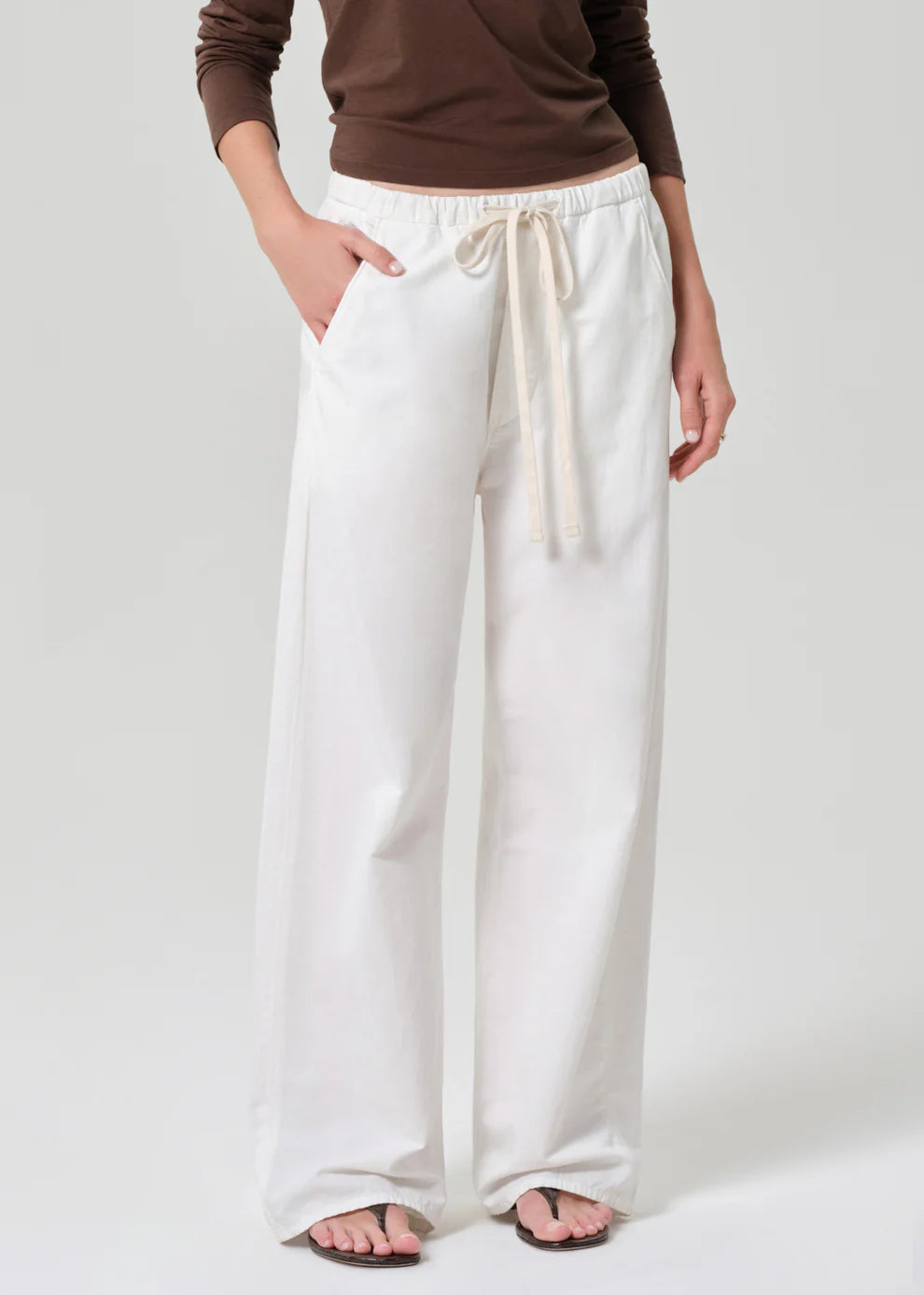 Person wearing white wide-leg pants with a brown top on a light gray background