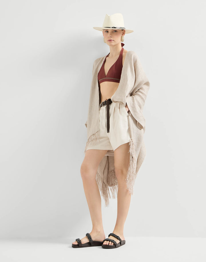 Woman wearing a beige cardigan, red top, and shorts with a white hat on a light gray background