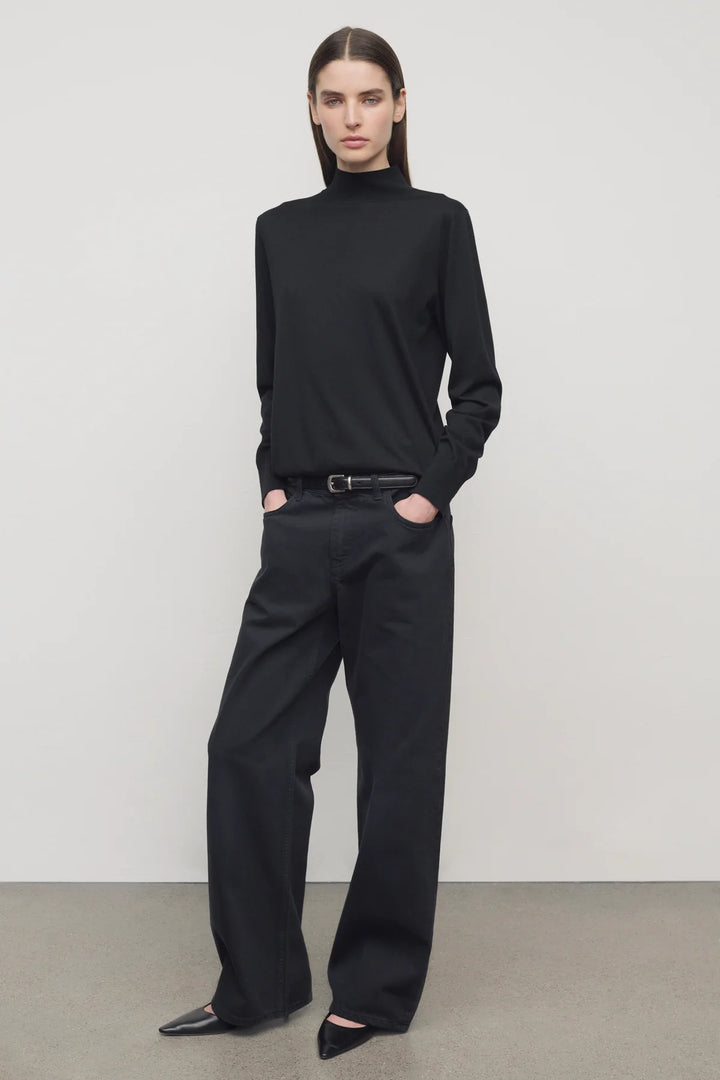 Person wearing a black turtleneck and wide-leg pants against a plain background