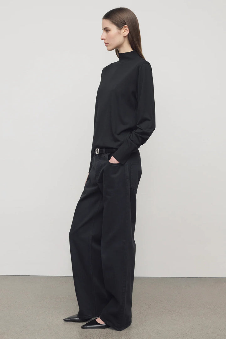 Person wearing a black outfit standing against a plain background