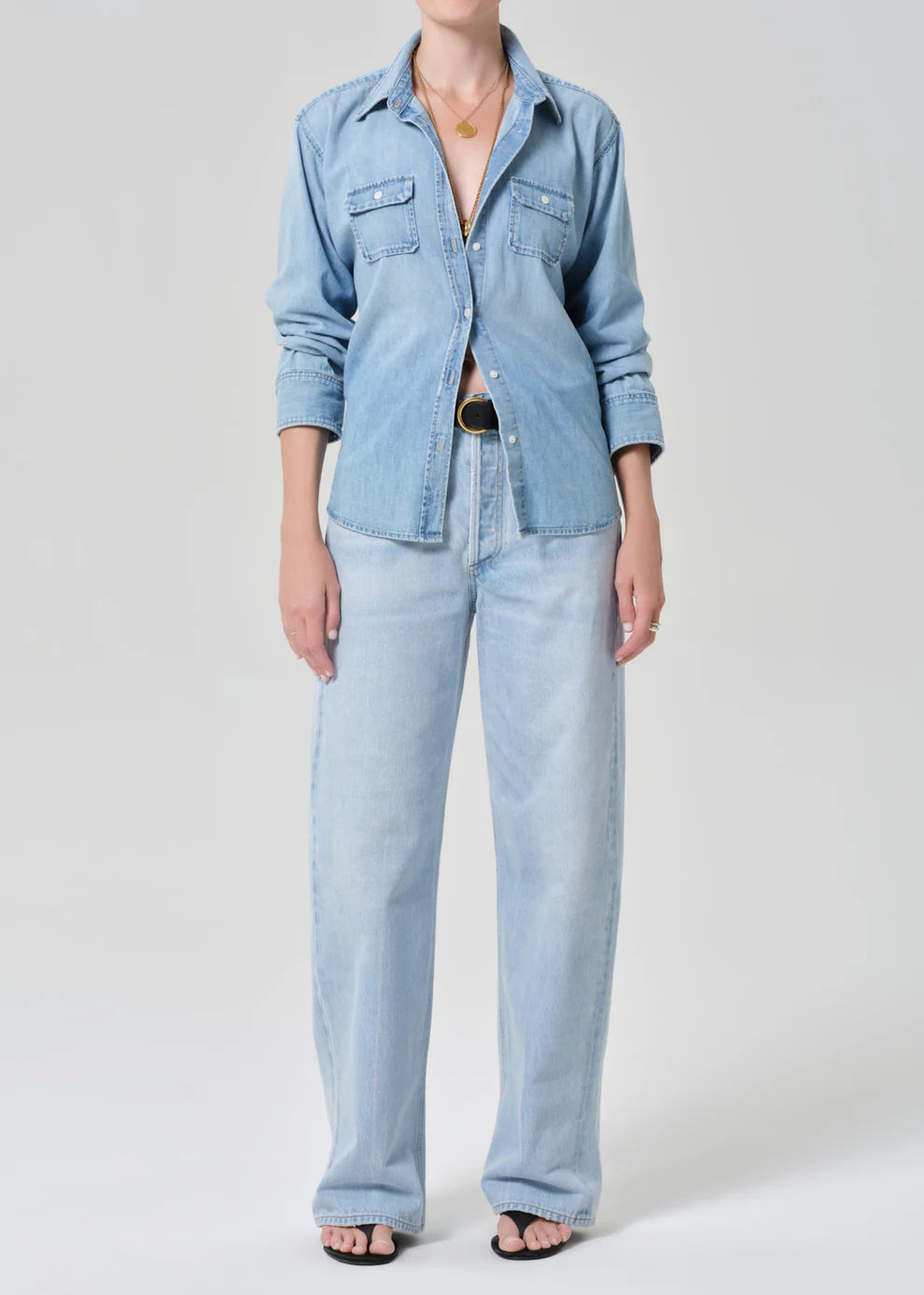 Person wearing a light blue denim shirt and jeans on a plain background