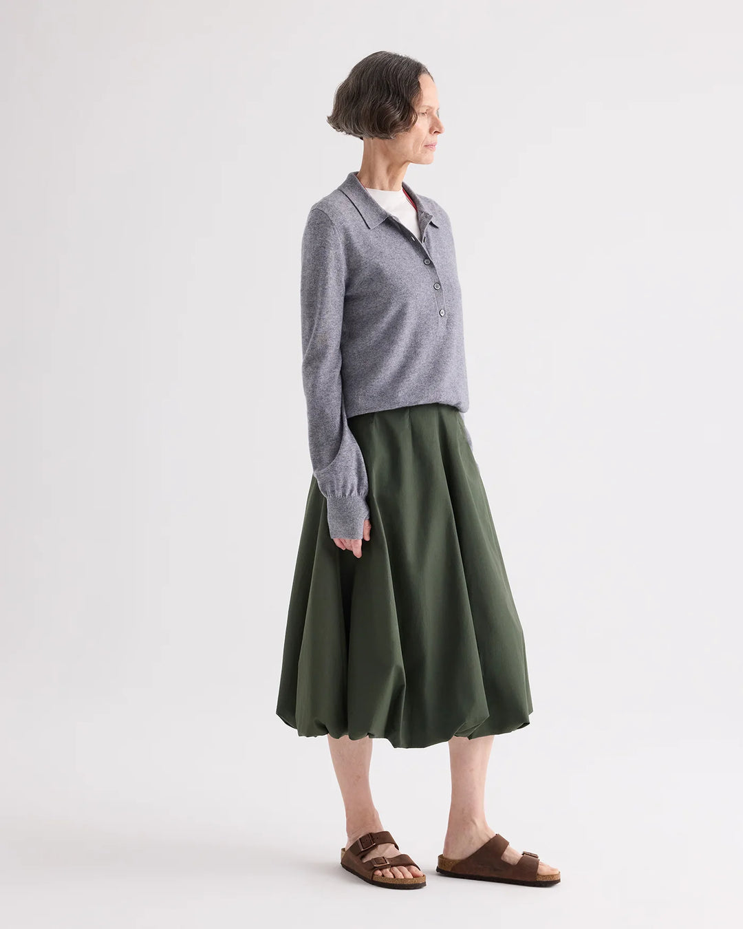 Person wearing a gray sweater and green skirt on a white background