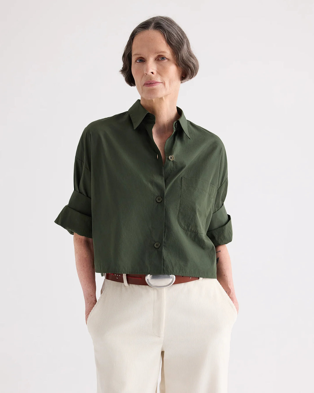 Woman wearing a green shirt and white pants on a plain background