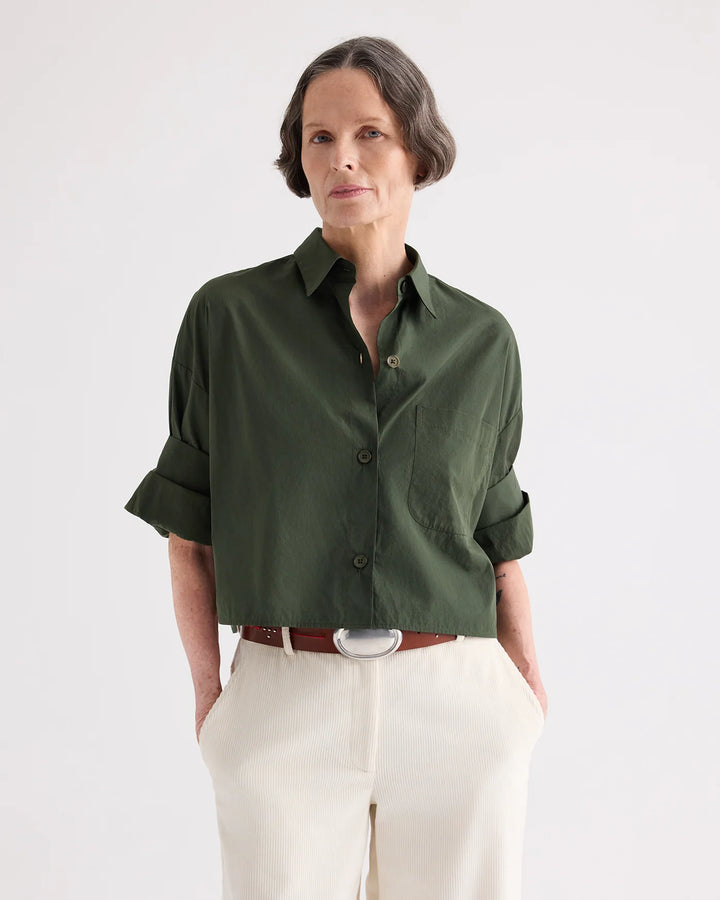Woman wearing a green shirt and white pants on a plain background