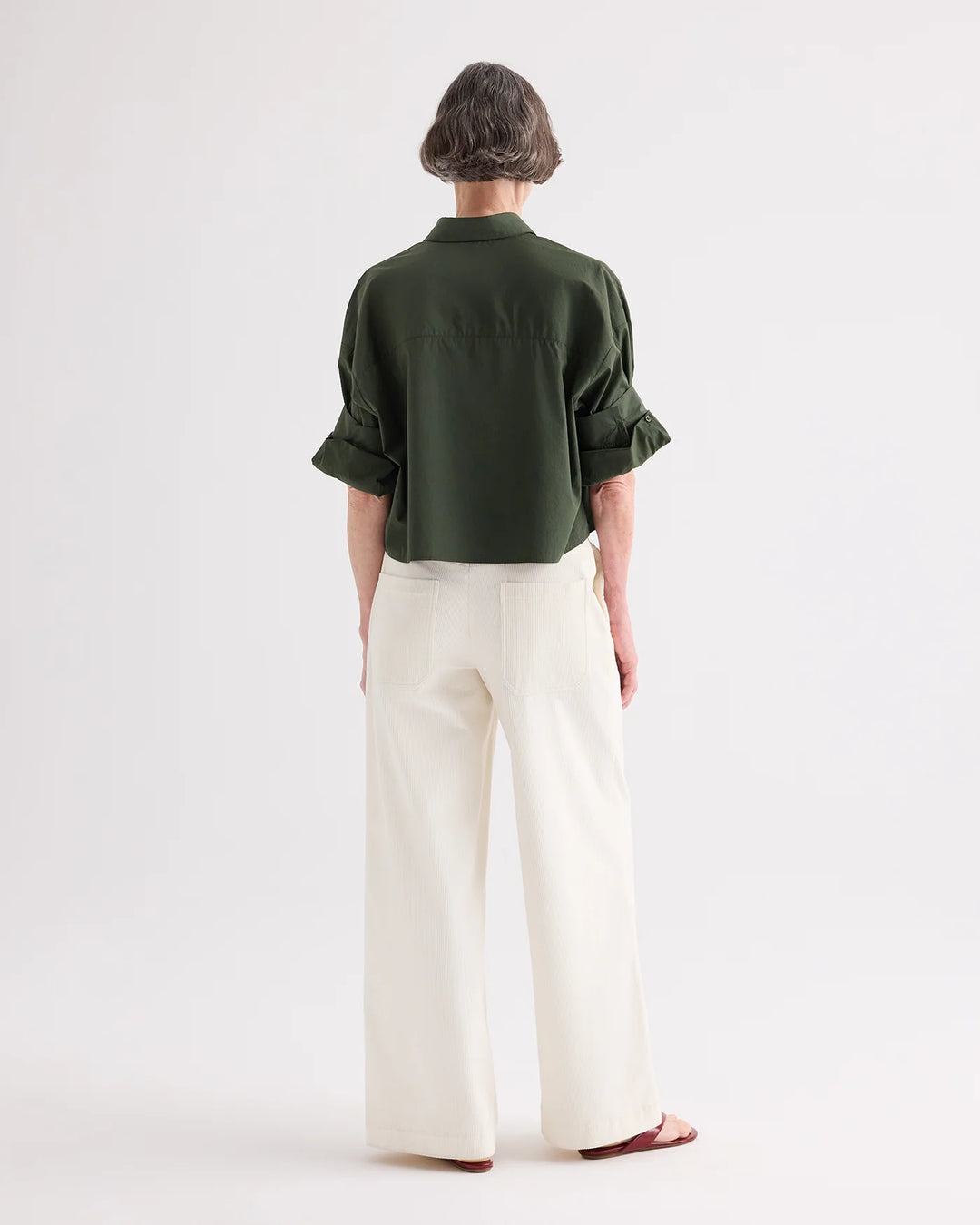 Person wearing a green shirt and white pants on a white background