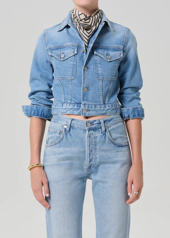 Person wearing a blue denim jacket and jeans on a plain background