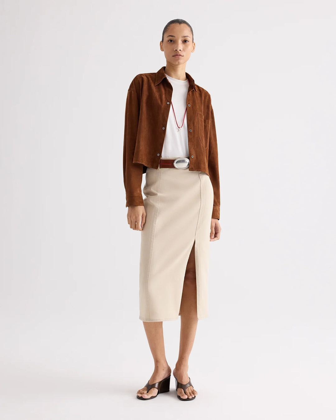 Woman wearing a brown jacket, white shirt, and beige skirt on a white background