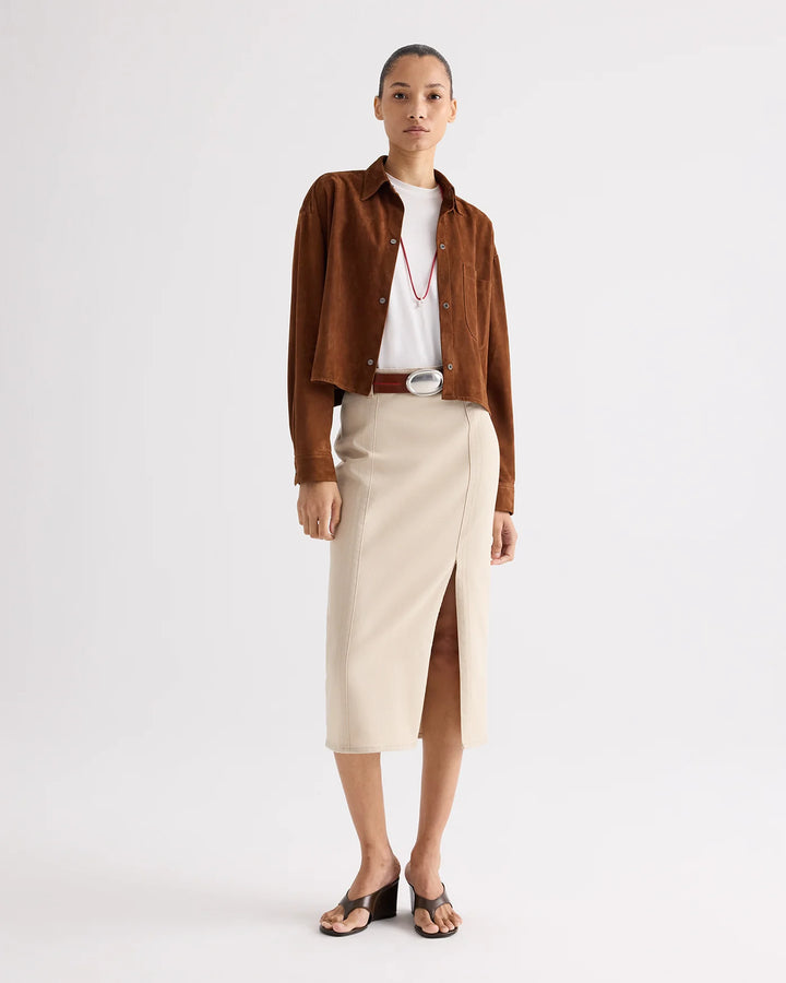 Woman wearing a brown jacket, white shirt, and beige skirt on a white background