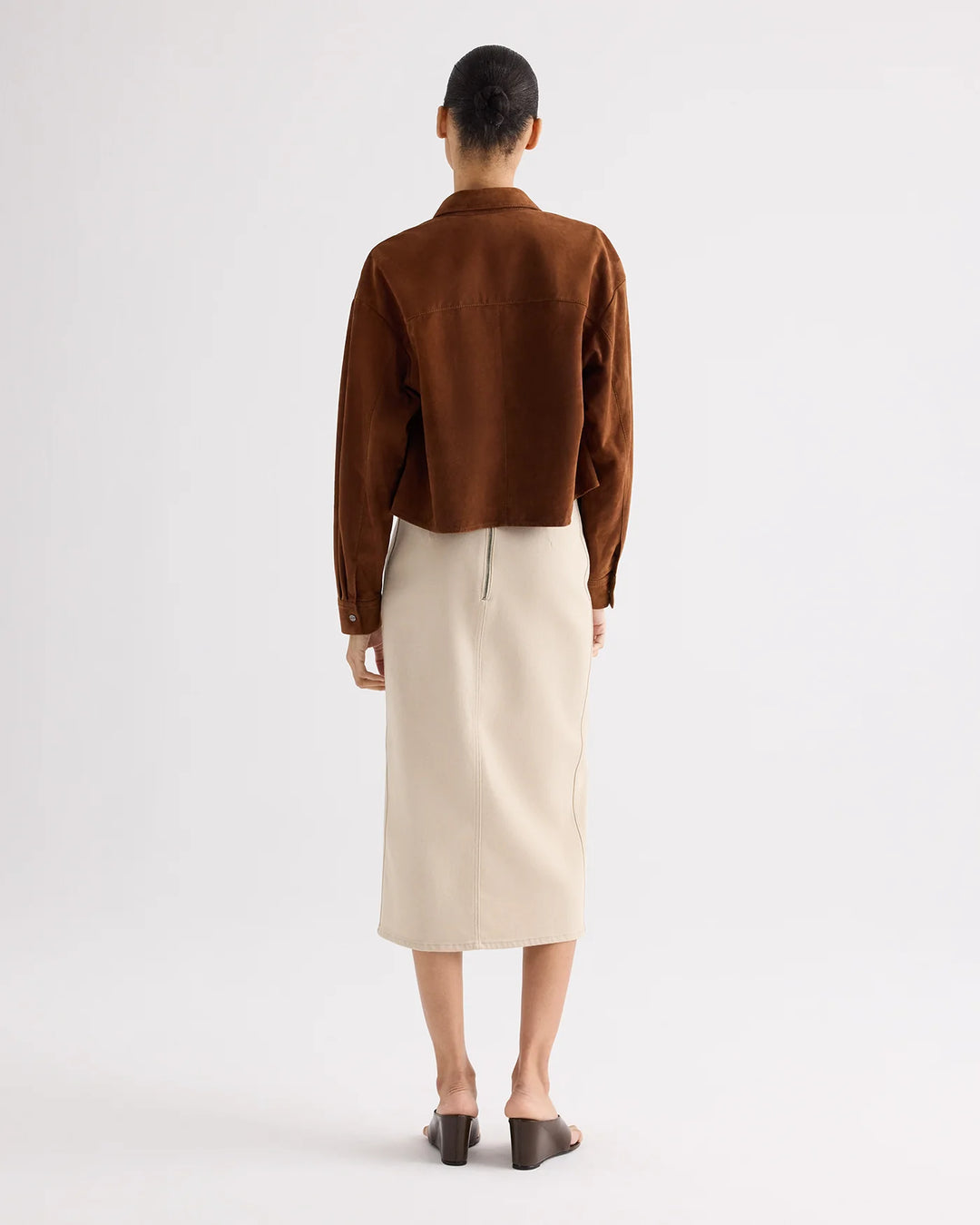 Person wearing a brown jacket and beige skirt on a white background