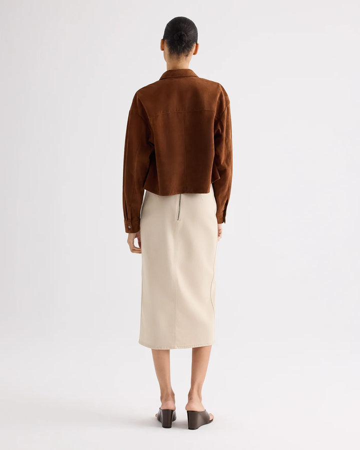 Person wearing a brown jacket and beige skirt on a white background