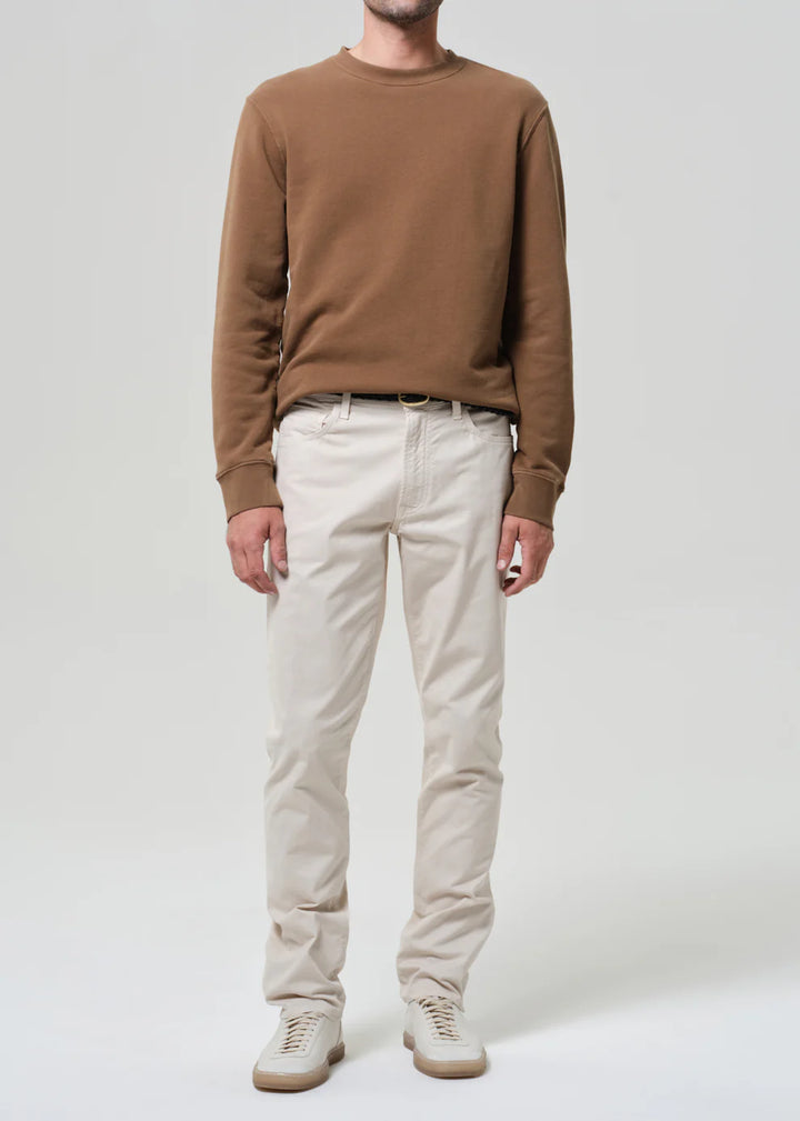 Person wearing a brown sweater and white pants on a plain background