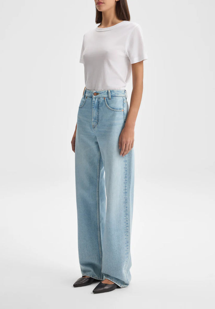 Woman wearing light blue jeans and a white top on a plain background