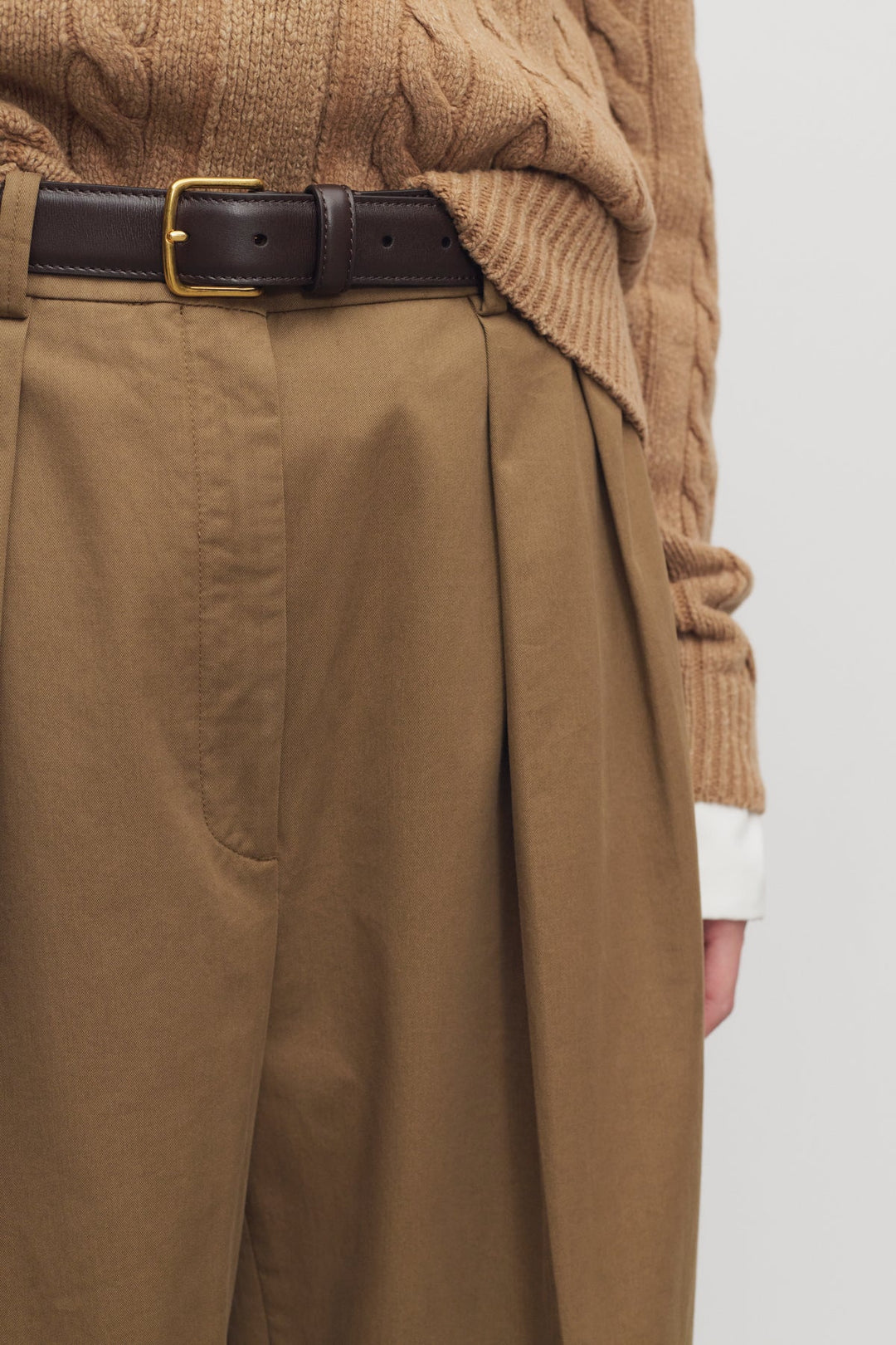 Person wearing a brown sweater and tan pants with a white background