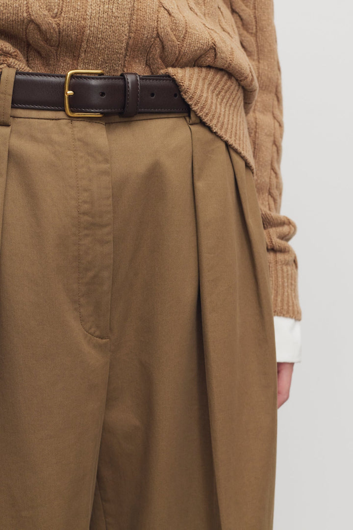 Person wearing a brown sweater and tan pants with a white background