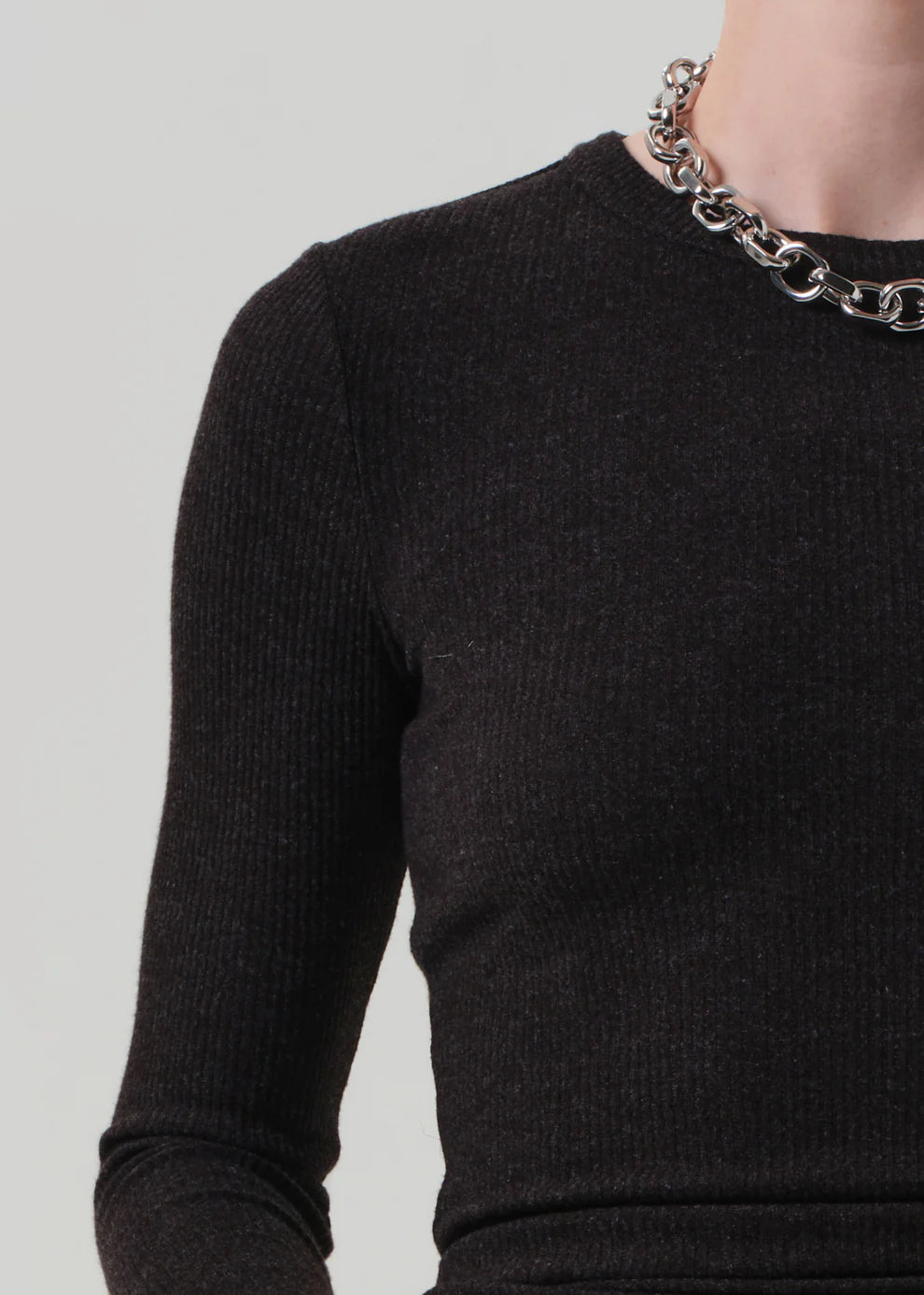 Person wearing a black sweater with a chain necklace on a light gray background