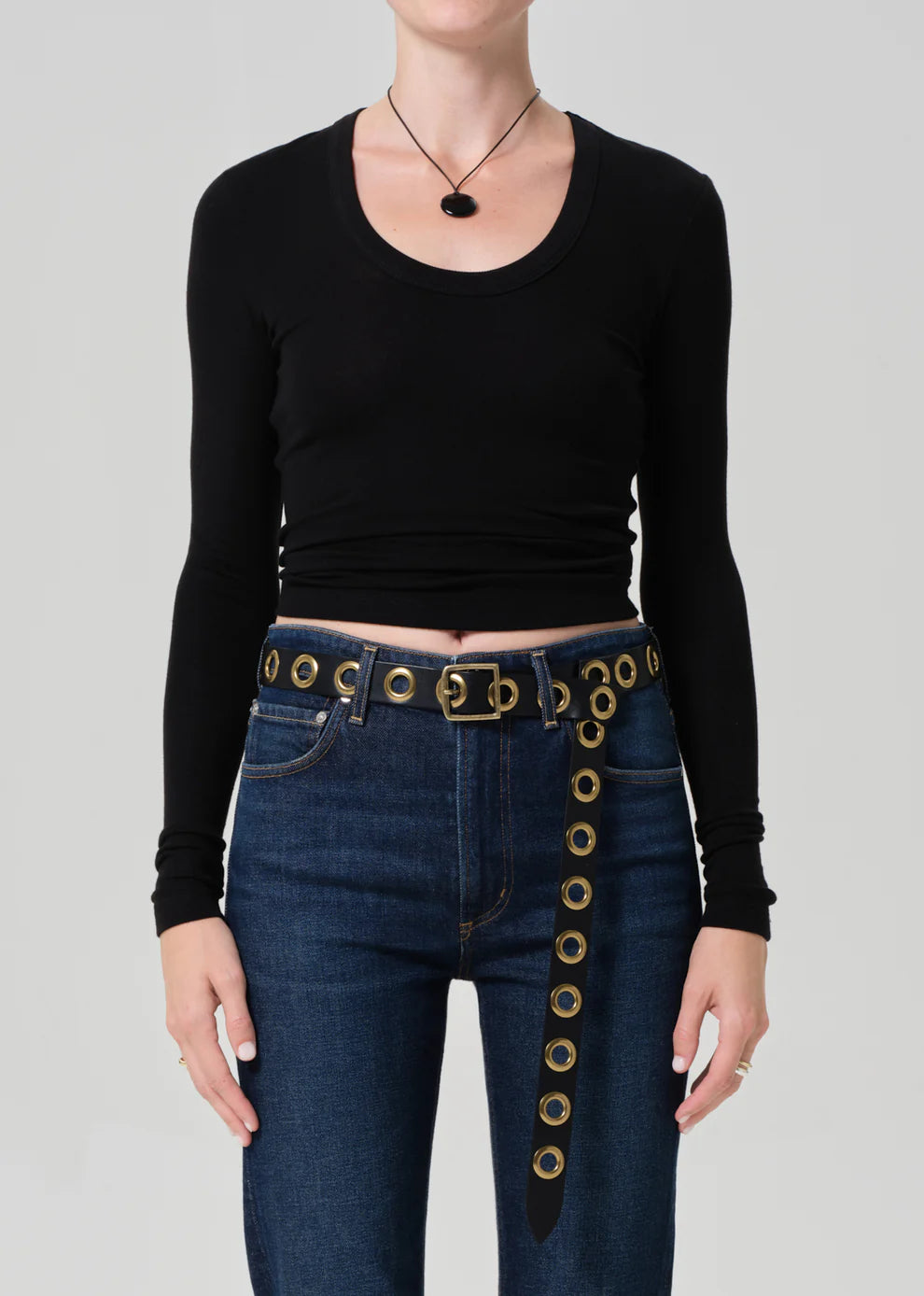 Person wearing a black long-sleeve top and blue jeans with gold belt buckle on a gray background