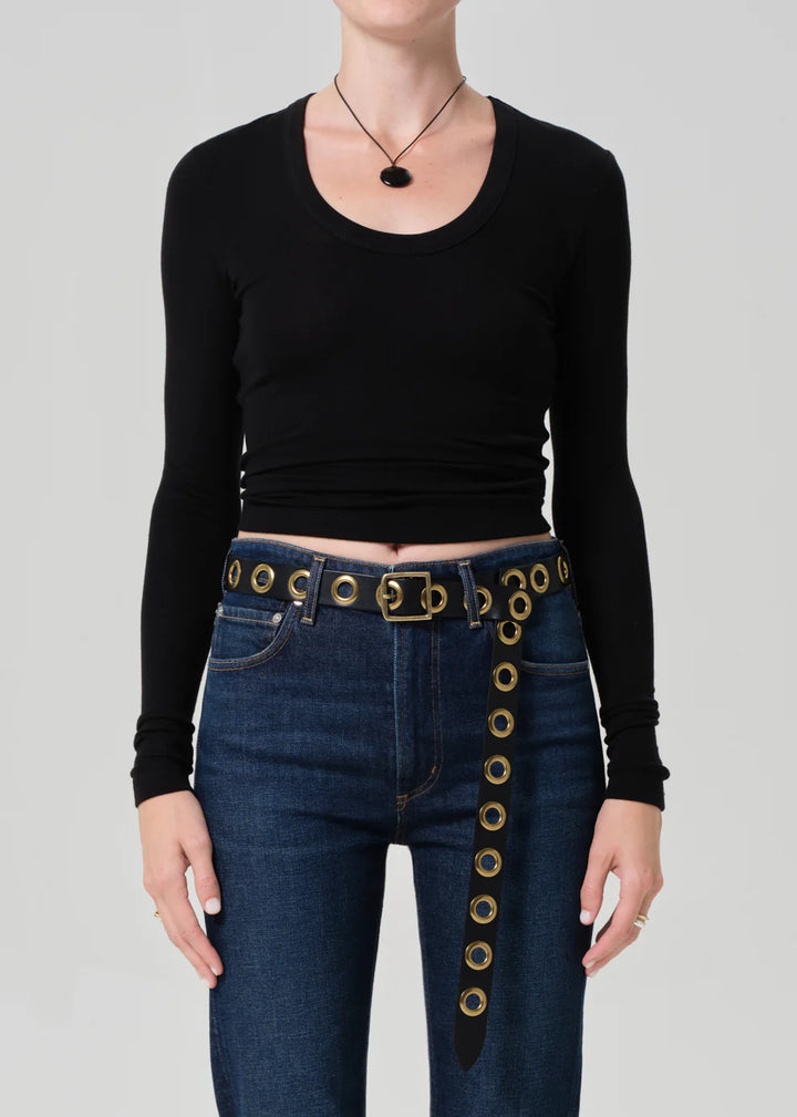 Person wearing a black long-sleeve top and blue jeans with gold belt buckle on a gray background