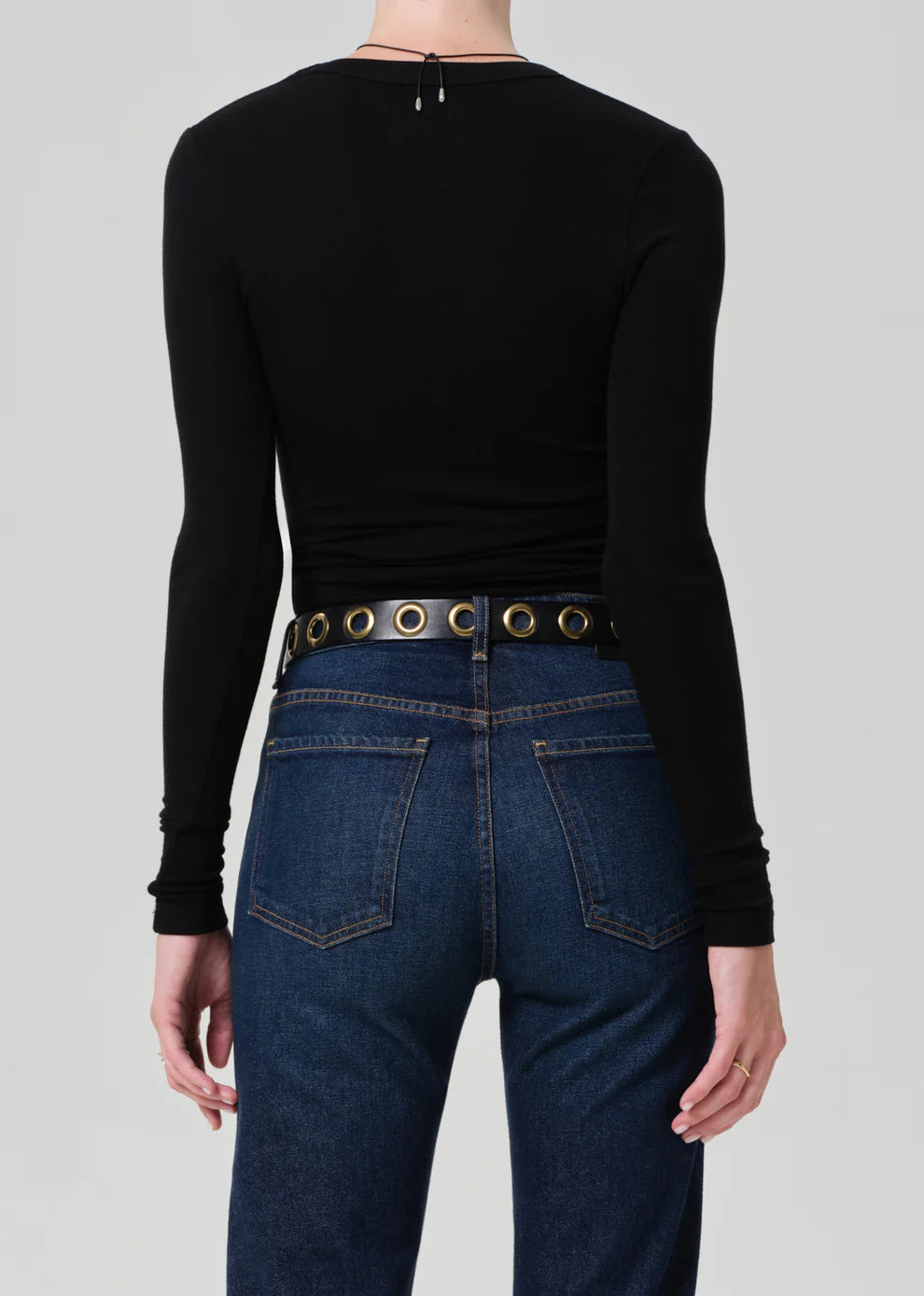Person wearing a black long-sleeve top and blue jeans with a belt on a gray background