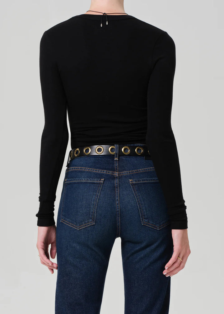 Person wearing a black long-sleeve top and blue jeans with a belt on a gray background