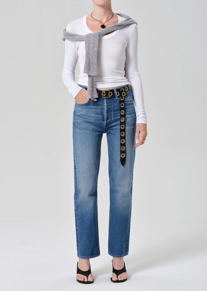 Person wearing a white long-sleeve shirt, gray cardigan, blue jeans with a decorative belt, and black sandals on a white background.