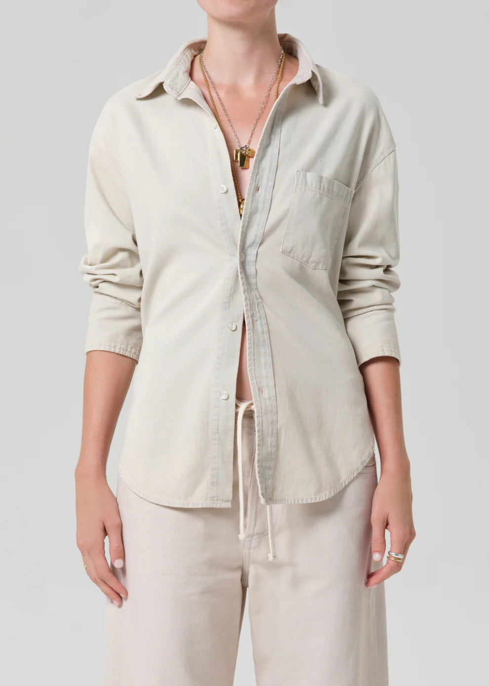 Person wearing a beige button-up shirt and pants on a plain background