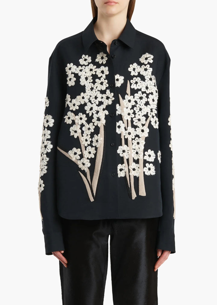 Black shirt with white floral patterns worn by a person on a white background