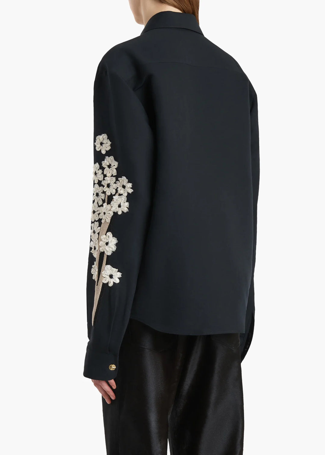 Black shirt with floral embroidery on sleeves worn by a person against a white background