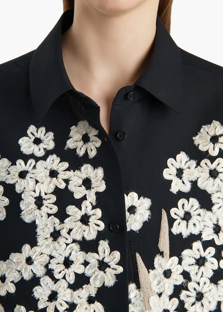 Black shirt with white floral embroidery on a plain background