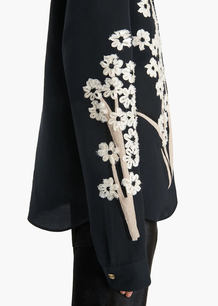 Black garment with white floral embroidery on a plain background