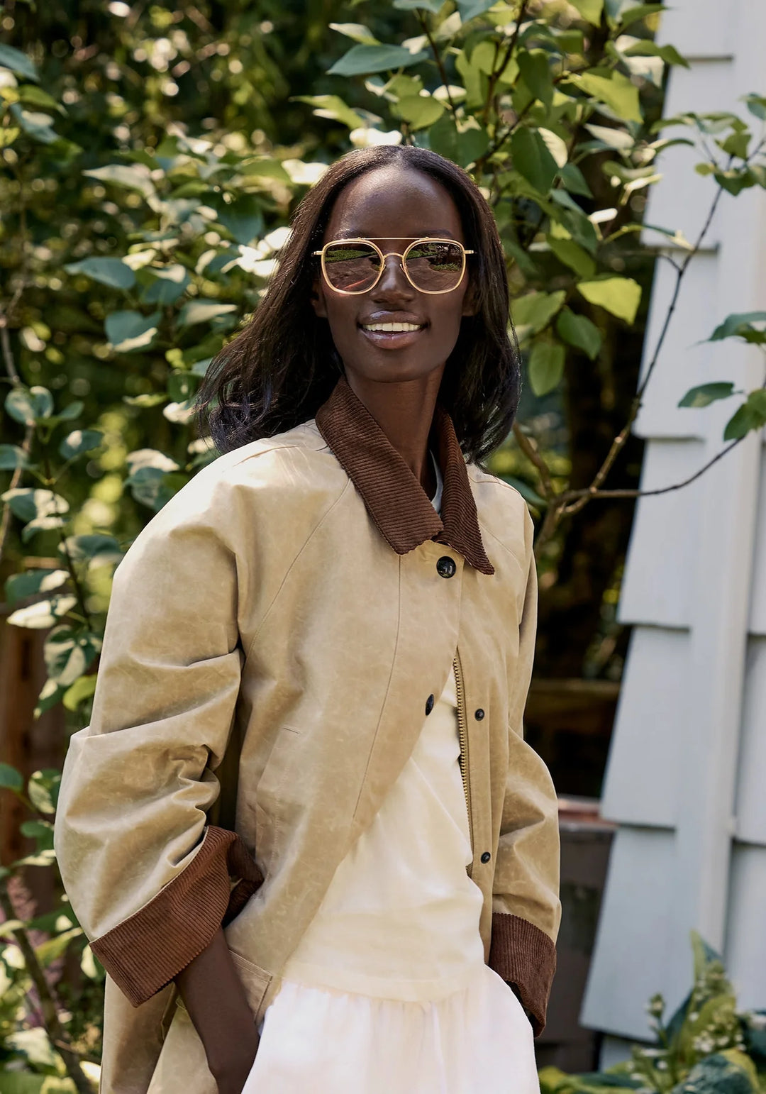 Woman wearing a beige coat with brown accents and sunglasses outdoors.