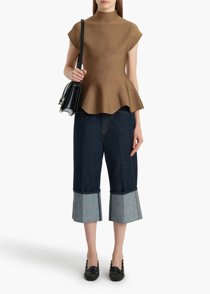 Woman wearing a brown top and dark blue jeans with a black handbag on a white background