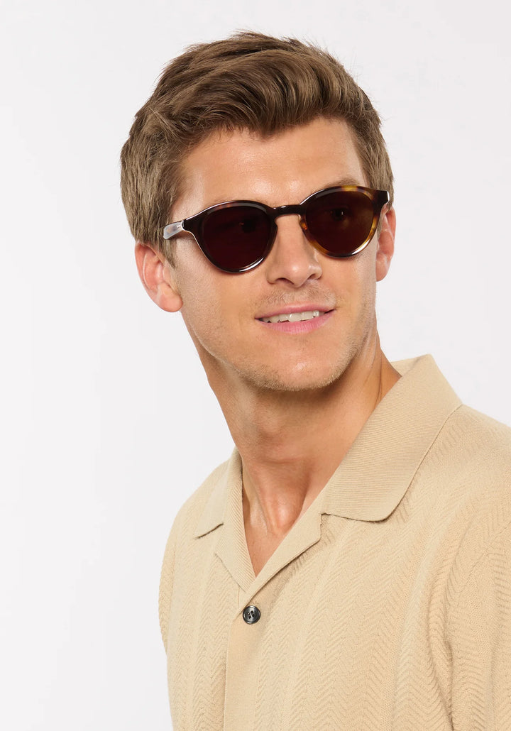 Man wearing sunglasses and a beige shirt against a white background