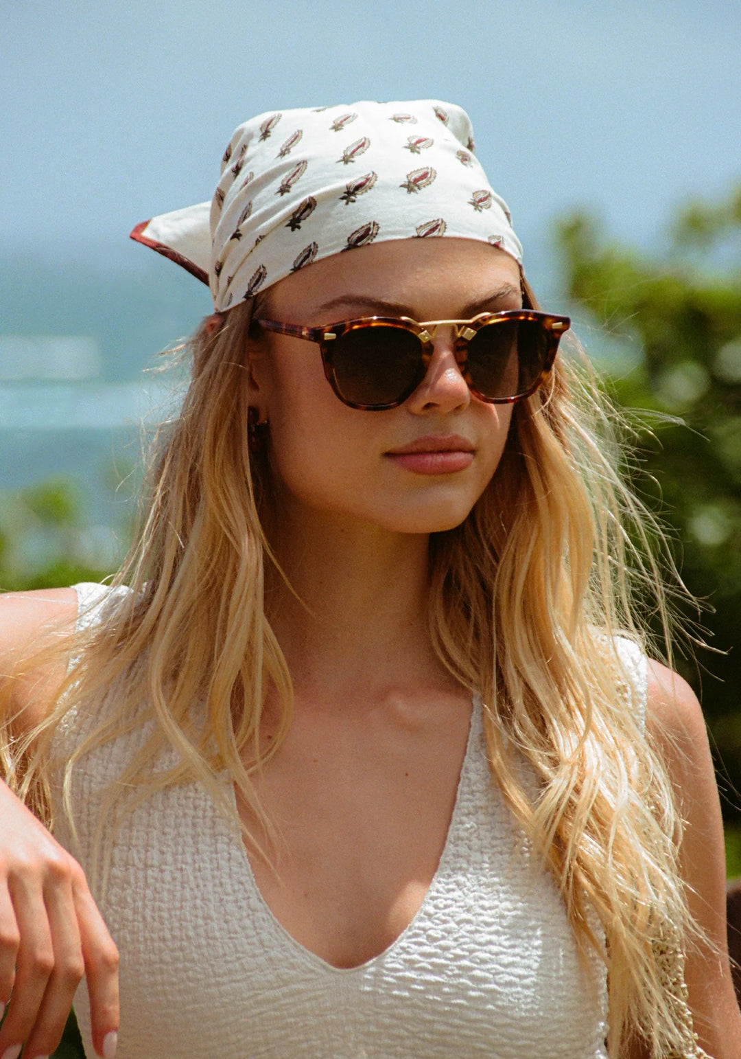Woman wearing sunglasses and a headscarf with a scenic background
