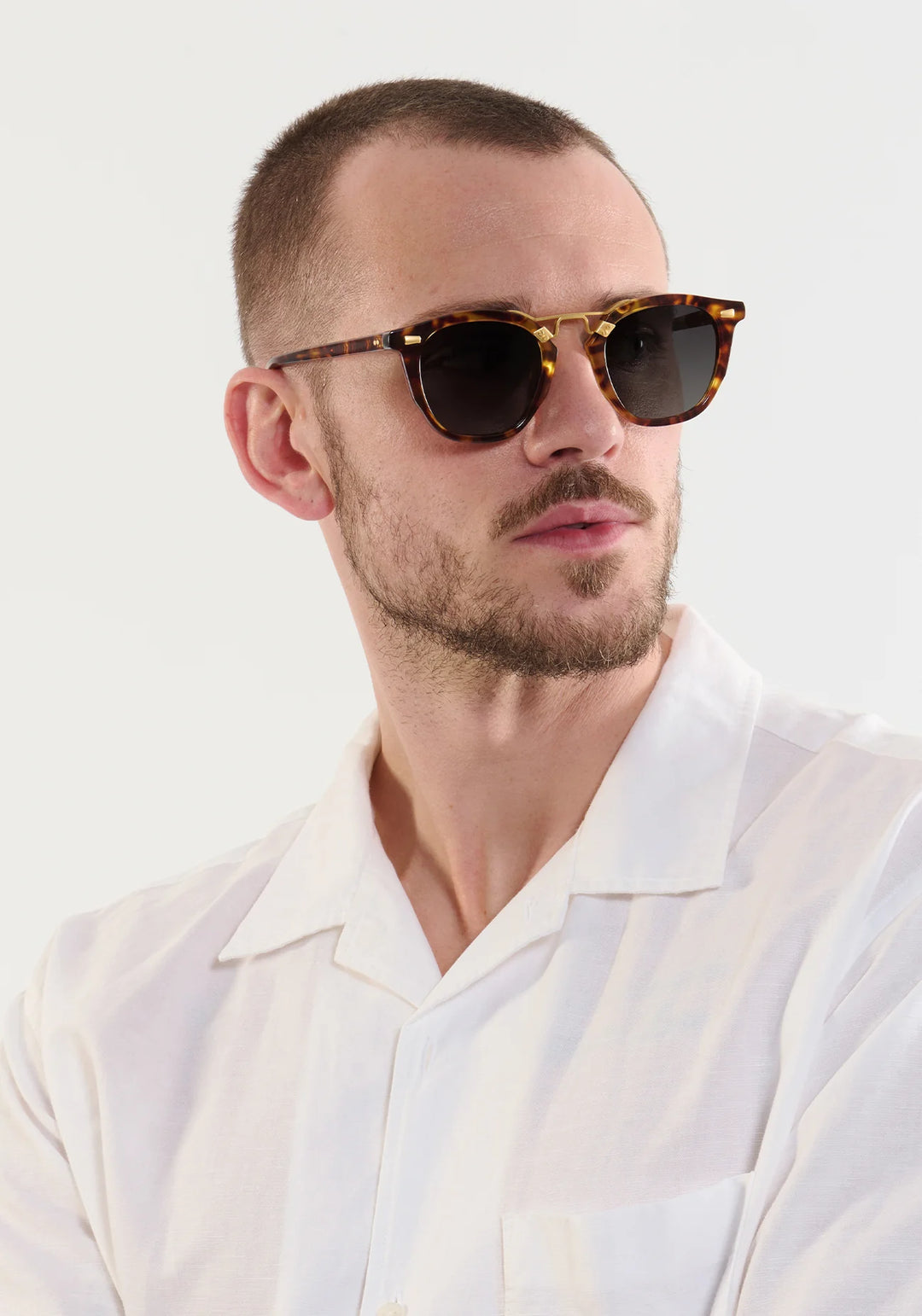 Man wearing a white shirt and tortoiseshell sunglasses against a white background