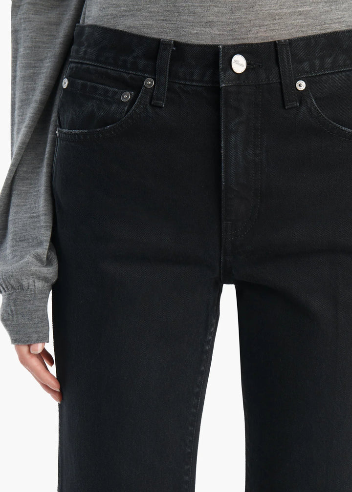 Close-up of a person wearing black denim jeans with a gray long-sleeve top, showing the waistband, front pockets, and button details.