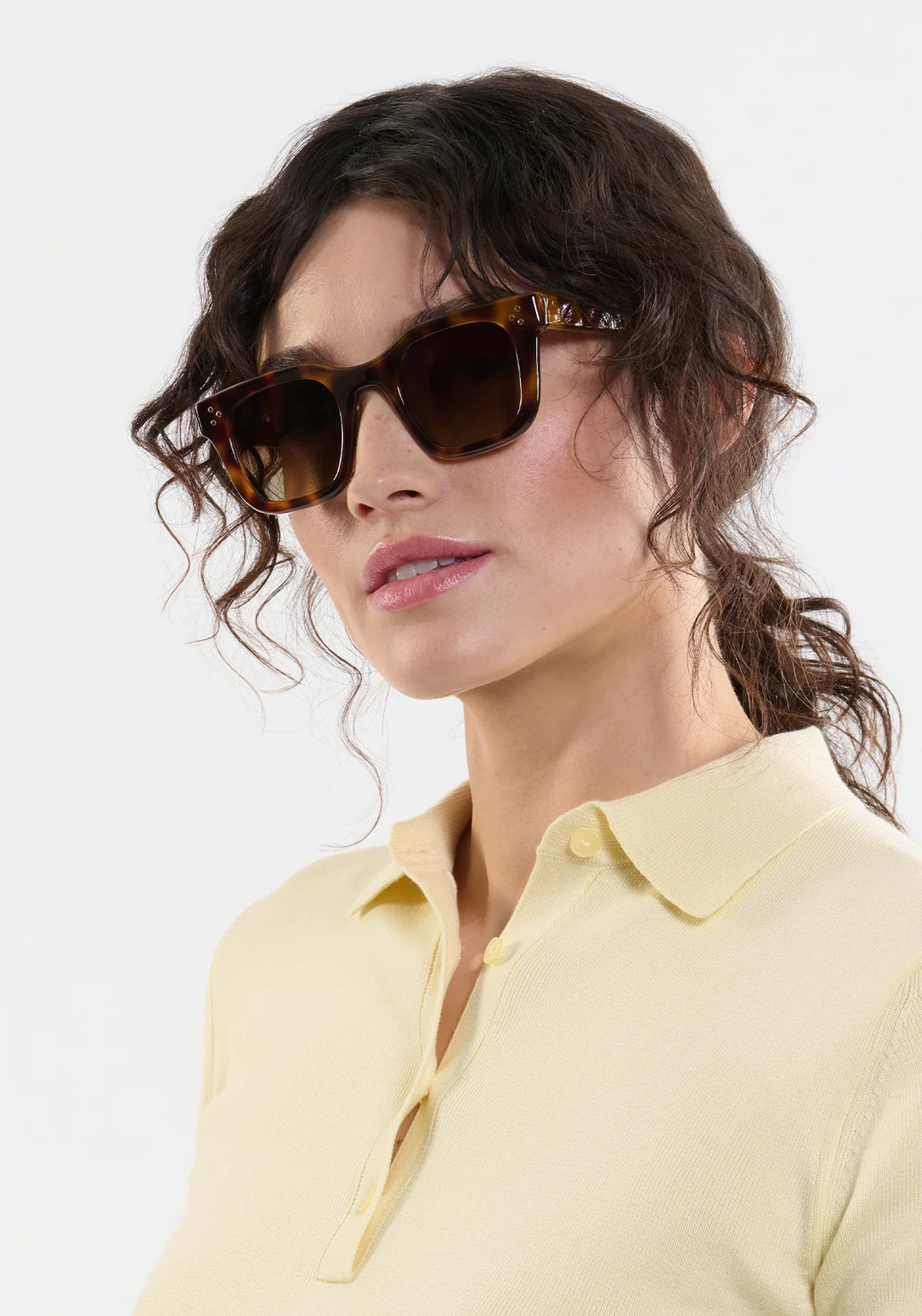 Woman wearing sunglasses and a yellow polo shirt against a light background
