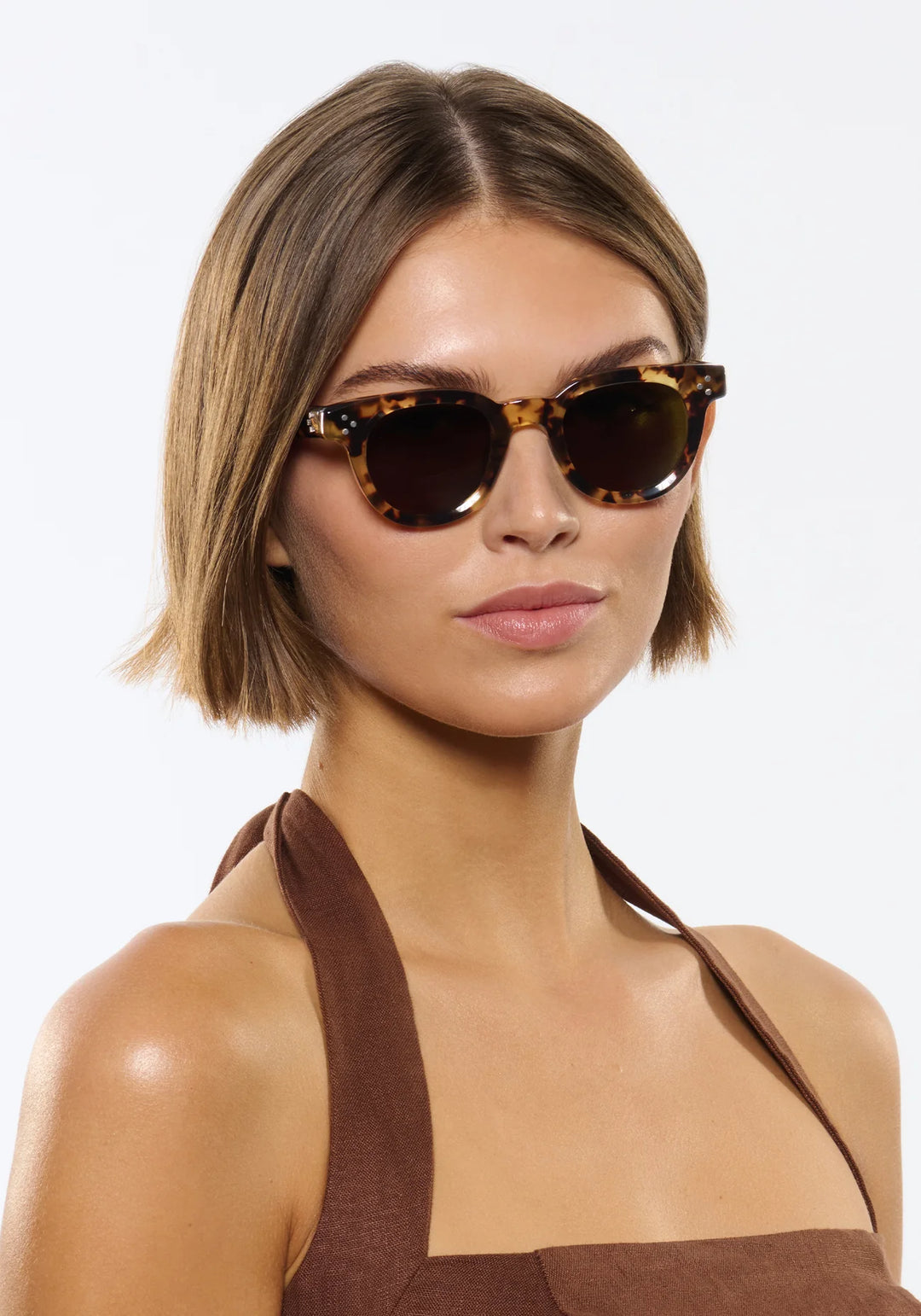 Woman wearing tortoiseshell sunglasses against a white background