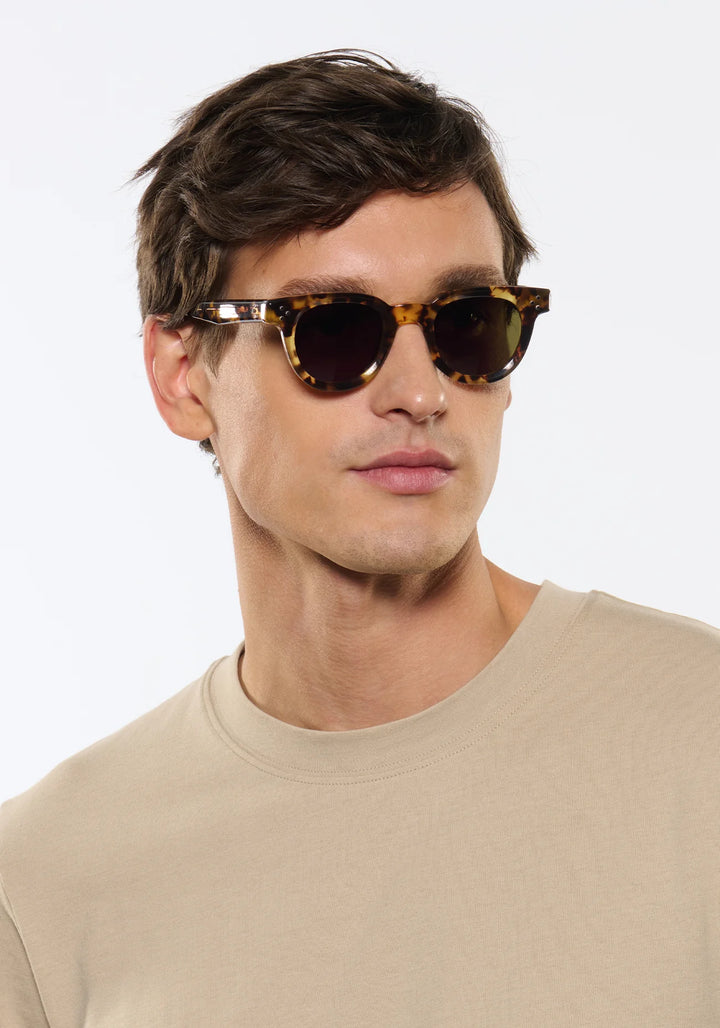 Man wearing tortoiseshell sunglasses against a plain background