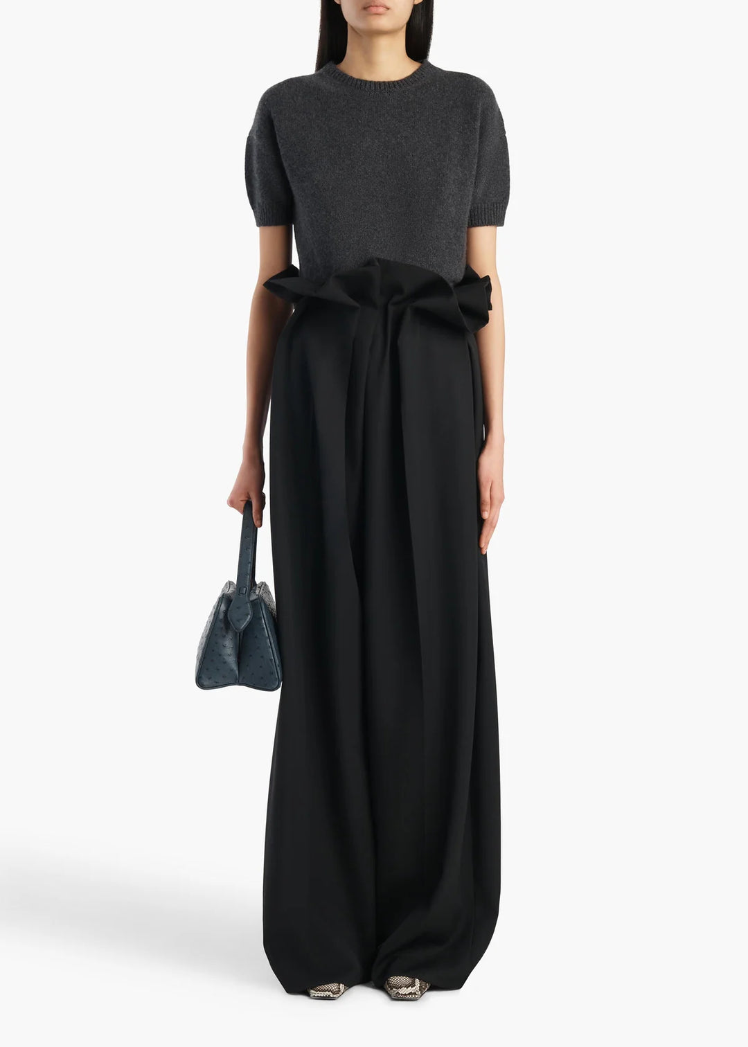 Woman wearing a black dress with a large bow and holding a matching handbag on a white background