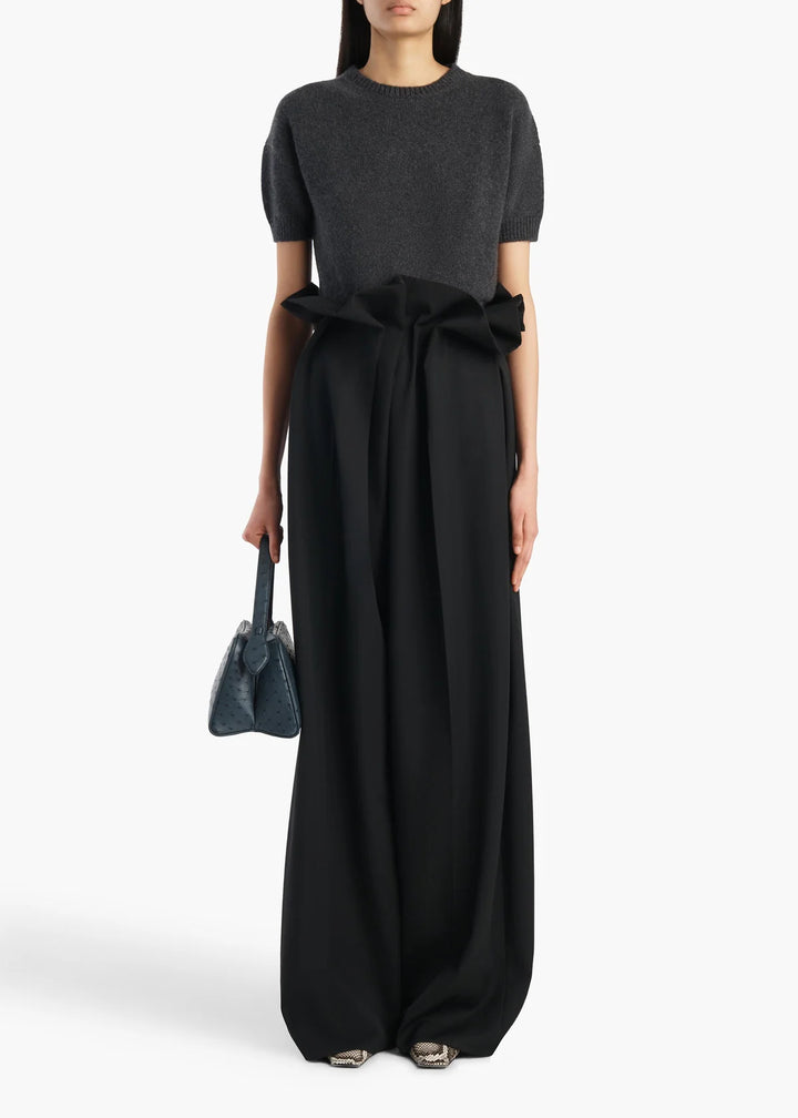 Woman wearing a black dress with a large bow and holding a matching handbag on a white background