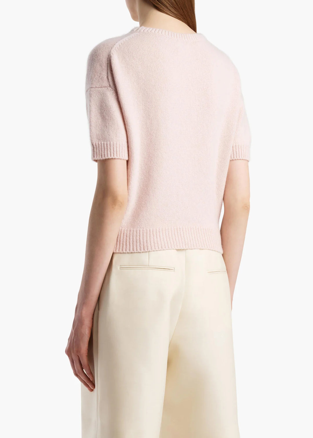 Person wearing a light pink short-sleeve sweater and beige pants on a white background